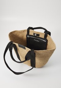Woven straw tote bag with black fabric straps and interior zip pouch. Features a circular base and textured surface. Black accents visible.