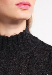 Pullover lavorato a maglia scuro con colletto alto, caratterizzato da un motivo testurizzato e perline decorative sottili lungo il colletto.