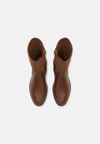 Bottes de cheville en cuir brun avec un dessus en tissu tan doux, dotées d'une fermeture éclair sur le côté et d'un design à bout arrondi. Texture lisse tout au long.