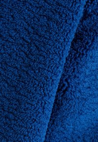 Modrá fleecová látka s texturovaným, nadýchaným povrchem; má hlubokou, sytou barvu a měkké, kadeřavé vlákna, což vytváří teplý vzhled.
