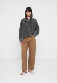 Gray corduroy cropped jacket with two chest pockets, paired with loose brown trousers and light pink flats. Set against a white background.
