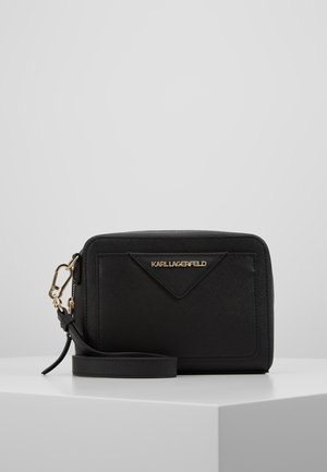 Sort Karl Lagerfeld håndledspung med gyldent logo, aftagelig rem og lynlås, placeret på en hvid geometrisk overflade.