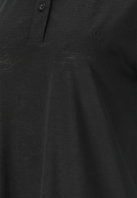 Svart polo-shirt i lätt tyg, med knappslå, korta ärmar och diskret logotyp på bröstet.