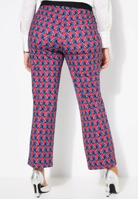 Pantalones con un patrón que presenta un audaz diseño geométrico en rojo, azul y blanco, con una cinturilla negra y una silueta ajustada. Tacones plateados complementan el look.