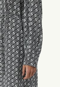 Langarmhemd aus schwarzem und weißem Stoff mit einem sich wiederholenden Logomuster. Das Material wirkt glatt mit einem leichten Glanz.