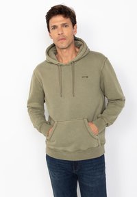 Oliwkowa bluza z kapturem, wykonana z miękkiego, strukturalnego materia�łu, z kieszenią typu kangaroo i ściągaczami przy nadgarstkach. Posiada sznurki w kapturze oraz subtelne logo.