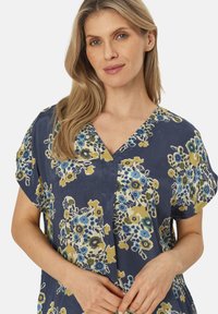 Blouse florale avec un fond marine, manches courtes et décolleté en V. Présente des fleurs colorées en bleu et jaune, avec une coupe décontractée.