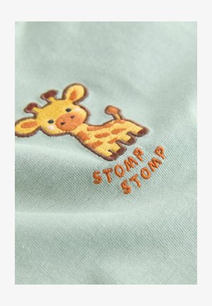 Svetlozelená tkanina s vyšívanou žirafou v žltej a hnedej farbe a nápisom "STOMP STOMP" v oranžovej farbe pod ňou. Mäkká textúra.