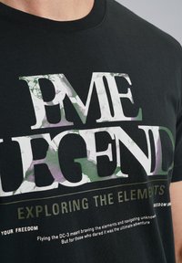 Čierne bavlnené tričko s veľkým bielym a zeleným textom "LEGEND" s abstraktnými vzormi a menším textom nižšie. Klasický dizajn s okrúhlym výstrihom.