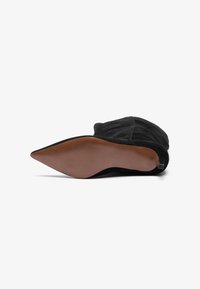 Stivaletto alla caviglia in suede nero con punta affusolata, suola piatta e una texture sottile. Presenta un tacco basso e un design pulito.