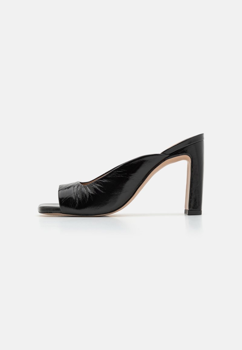 Mule à bout ouvert en cuir verni noir avec un talon épais haut et une semelle lisse couleur tan sur fond blanc.