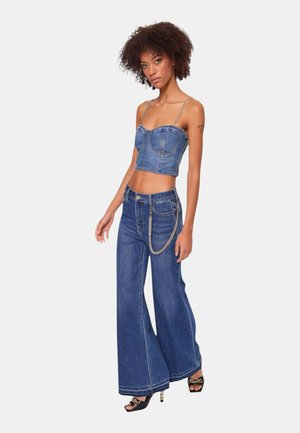 Top corto in denim con spalline a catena, corpino aderente, abbinato a jeans a gamba larga in denim con un accento a catena in vita. Lavaggio blu.