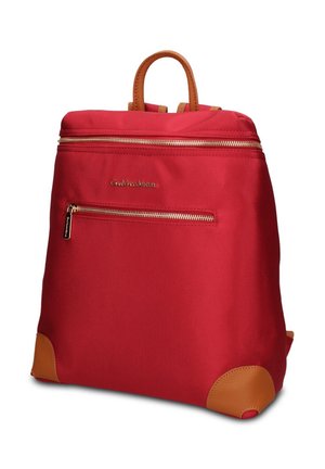 Sac à dos en tissu rouge avec accents en cuir marron, poignée supérieure, poche avant zippée et fermetures éclair dorées sur fond blanc.