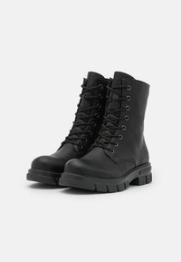Botas de cuero negro hasta el tobillo con punta redonda, cierre de cordones en la parte delantera y suela de goma gruesa con patrones de tracción.