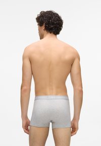 Szürke pamut boxeralsó, puha rugalmas derékkal, amelyen a "KARL LAGERFELD" logó látható, hátulról nézve. A bőr a derékpánt felett látható.