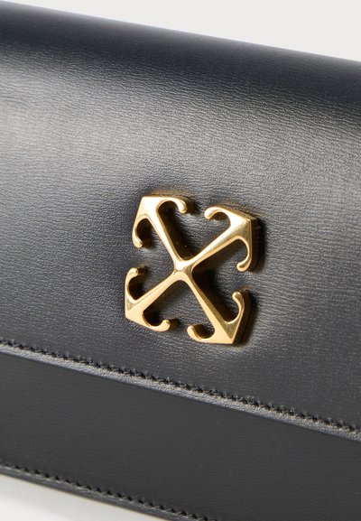 Μαύρη επιφάνεια από δέρμα με ένα χρυσό διακοσμητικό έμβλημα σε σχήμα τεσσάρων βελών που δείχνουν προς τα έξω σε συμμετρικό σχέδιο.