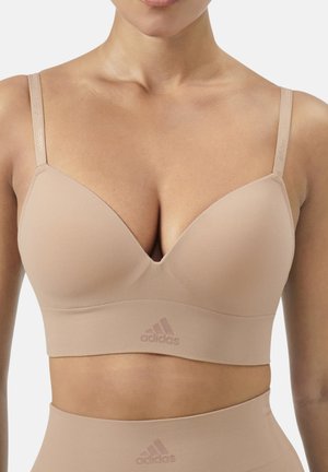 Femme portant un brassard de sport Adidas beige à fines bretelles et un legging taille haute, montrant le torse du cou à la taille.