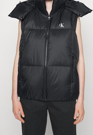 Mouwloos zwart puffervest met een ritssluiting aan de voorkant, ritszakken aan de zijkanten, een hoge kraag en een wit "cK"-logo op de linkerborst.