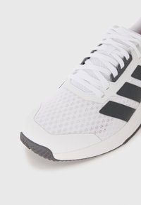 Scarpa sportiva bianca con tomaia in rete, accenti neri e logo a tre strisce. La suola presenta una presa strutturata e un design elegante e moderno.