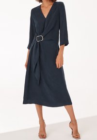 Navy Wickelkleid mit V-Ausschnitt, Dreiviertelärmeln und einem vorderen Knoten, der mit einer goldenen Schnalle gesichert ist, mit einer fließenden Textur und Midi-Länge.