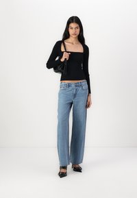 Black ribbed long-sleeve top with square neckline, paired with light blue wide-leg jeans. Black bag with strap and pointed heels with accents.