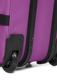 Purple suitcase with a textured fabric surface, black plastic accents, and two durable wheels, featuring a reinforced base and robust zipper.