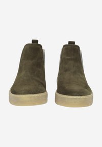 Botas de tobillo de ante verde oliva con paneles laterales elásticos y suelas de goma beige. Presenta costuras mínimas y una lengüeta en la parte posterior.