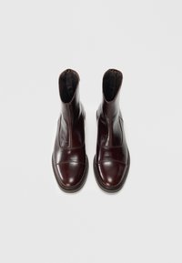Bottines en cuir marron avec une finition lisse, des bouts ronds, des panneaux latéraux élastiques et des semelles texturées, arborant un design minimaliste.