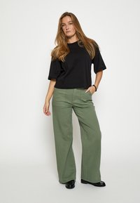 Melna īsā t-kreklā ar īsām piedurknēm, saskaņota ar augsto vidukli, plaša klāja oliīvzaļajām biksēm. Melni apavi piešķir komplektam pabeigumu.