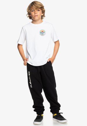Hvid t-shirt med rundt grafisk motiv, sorte sweatpants med hvidt logo, grå sneakers med gule accenter. Casual pasform med afslappet silhuet.