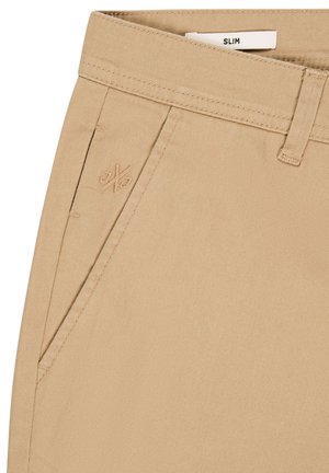 Schmale beige Baumwollhosen mit flachem Bund, seitlichen Taschen und dezent gesticktem Logo auf der Vorderseite. Glatte Textur.