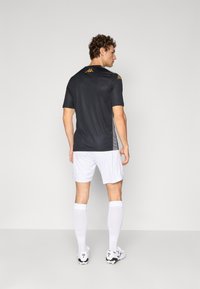 Maillot de sport à manches courtes noir avec logo doré, associé à un short et des chaussettes blanches. Design ajusté pour les activités sportives.