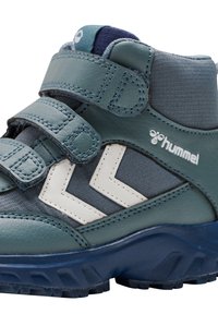 Mittelhohe Kinderschuhe aus dunkeltürkisfarbenem und grauem Synthetikmaterial, ausgestattet mit zwei Klettverschlussriemen, weißen Zickzackmustern und einer strukturierten Gummisohle.