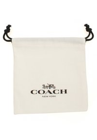 Bomullssnörväska i vitt med en svart logotyp som läser "COACH NEW YORK" och en illustration av en häst och vagn.