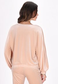 Top in velluto color pesca con maniche a palloncino, polsini ed elastico in vita. Texture liscia e morbida con una vestibilità rilassata.
