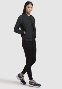 Giacca bomber navy con polsini a coste, abbinata a leggings neri e sneakers navy con logo bianco. Tessuto liscio e leggero.