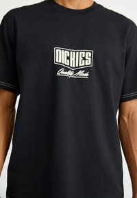 Maglietta nera in cotone con logo bianco recante la scritta "DICKIES" e "Quality Made". Maniche corte, scollo rotondo e cuciture a contrasto.