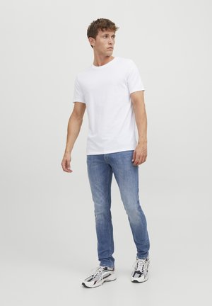 T-shirt bianco a maniche corte, jeans slim-fit azzurri, e scarpe da ginnastica multicolori. Design semplice e casual.