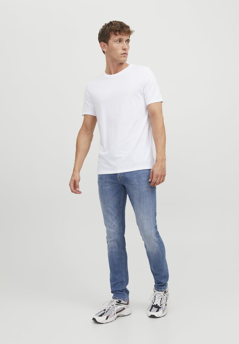 T-shirt bianco a maniche corte, jeans slim-fit azzurri, e scarpe da ginnastica multicolori. Design semplice e casual.
