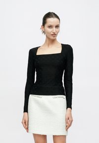 Μαύρο τοπ μακρυμάνικο με τετράγωνο ντεκολτέ και υφή, συνδυασμένο με λευκή μίνι φούστα με υφή και ασημένιες λεπτομέρειες.