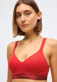 Rød bomulls-bralette med V-halsdesign, med justerbare stropper og en elastisk kant med logo. Glatt tekstur gjennom hele.