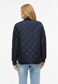 Temno modra prešita jakna z vzorcem diamantov, z rebrastimi manšetami in ovratnikom. Mehka tekstura, lahka zasnova in sproščen kroj.