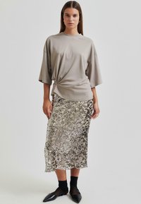 Siva oversize majica s čvorom spreda, uparen s mid-length suknjom srebrne boje s kristali. Crne cipele s oštrim vrhom i prozirne crne čarape.