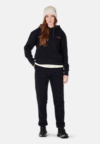 Zwart sweatshirt met een voorzak, gecombineerd met bijpassende zwarte sweatpants. Lichtkleurige gebreide beanie. Glad stoftextuur.