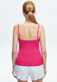 Top in cotone rosa aderente con spalline sottili, texture a coste, abbinato a pantaloni corti bianchi in pizzo con orlo sfilacciato e tasche posteriori.
