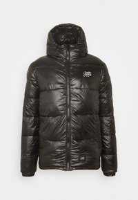 Veste noire matelassée avec une texture brillante et matelassée, fermeture éclair complète et capuche. Présente un petit logo sur le côté gauche de la poitrine.