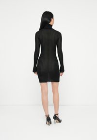 Μαύρο πλεκτό φόρεμα με ζιβάγκο, μακριά μανίκια και εφαρμοστή γραμμή. Τελειώνει πάνω από το γόνατο με κροκόδειλο στρίφωμα. Φοριέται με μαύρες ψηλές γόβες.