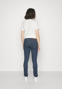 Smaljeans i mørkeblå denim med lærplakett bak. Kombinert med en hvit t-skjorte med korte ermer og hvite joggesko.