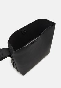 Černá kožená taška s měkkou texturou, otevřeným vrškem a vnitřní kapsou na zip. Vyznačuje se elegantním, minimalistickým designem. Součástí je nastavitelné ramenní popruhy.