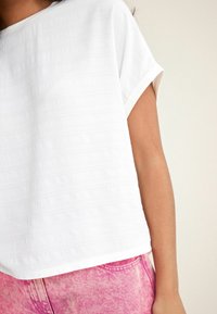Hvid tekstureret top med korte ærmer og rund halsudskæring, parret med lyserøde denimshorts med et falmet mønster.